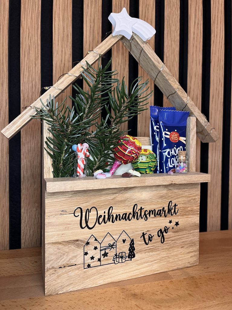 Hier ist ein aus HOlz gebastelter Mini-Weihnachtsmarktstand zu sehen, in dem Süßigkeiten angeboten werden. Es handelt sich um Deko.